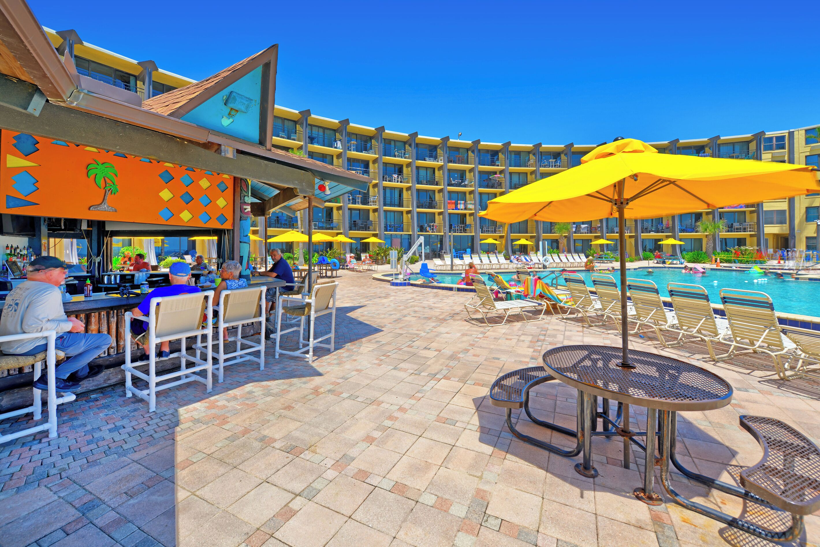 A hotel pool area with lounge chairs, umbrellas, and a bar.