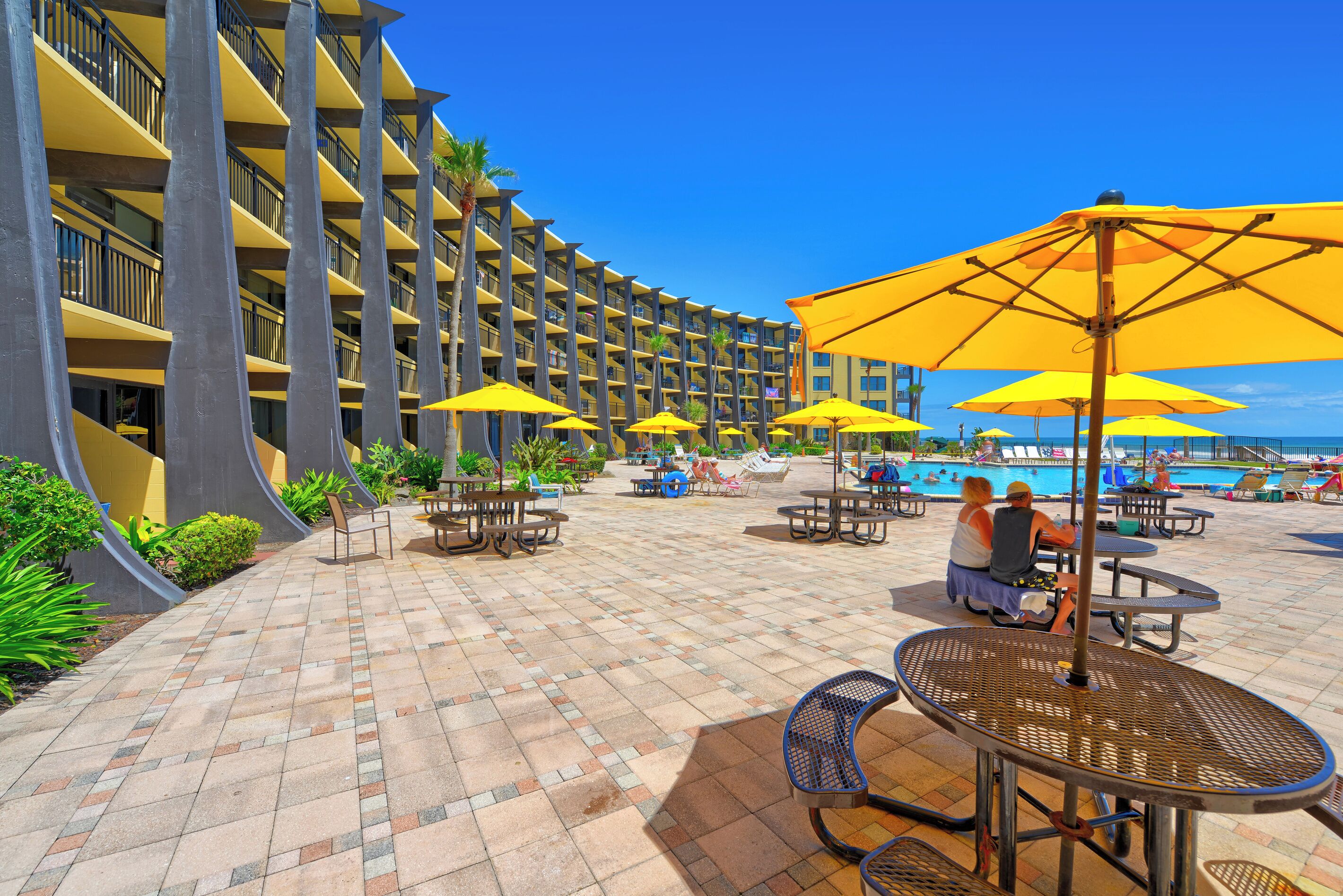 A hotel with a pool area, outdoor seating, and a view of the ocean.