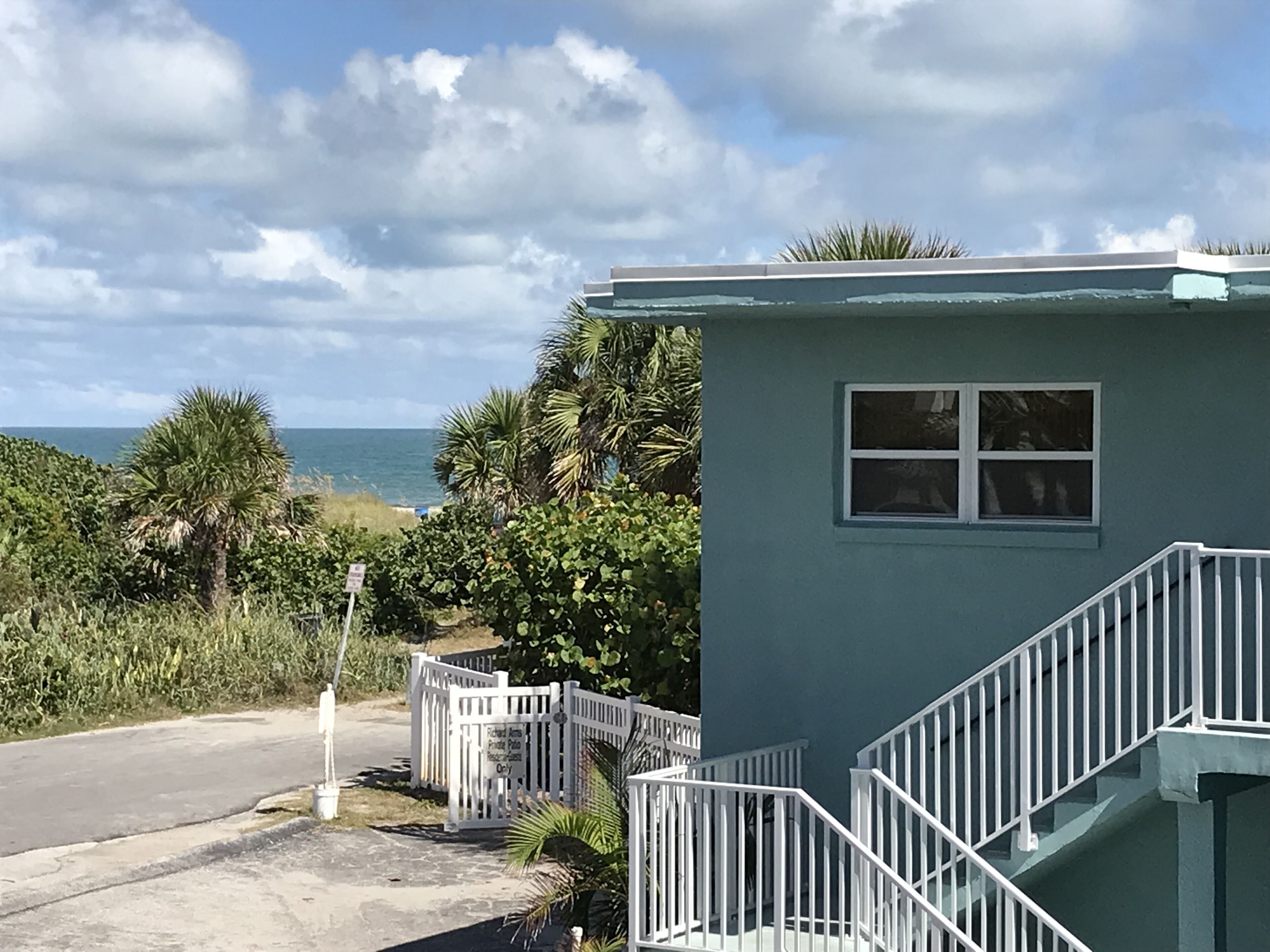 A small, single-story building with a white railing staircase, a window, and a sign indicating a private parking area.