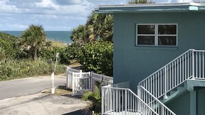 A small, single-story building with a white railing staircase, a window, and a sign indicating a private parking area. - Lovely Ocean Views! (Cocoa Beach)