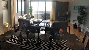A modern living room with a sofa, coffee table, and dining area. There is a balcony with a view, a fireplace, and a painting on the wall. - Luxury Ocean Front 2br/2ba Horizons Condo17th Floor - Awesome views (Daytona Beach)