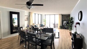 A spacious living room with a dining area, large windows, a ceiling fan, and a stone fireplace. - Luxury Ocean Front 2br/2ba Horizons Condo17th Floor - Awesome views (Daytona Beach)