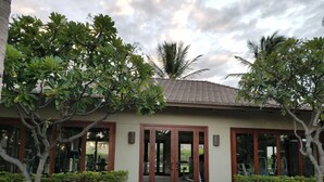 A building with a tiled roof, large glass doors, and a paved entrance area with surrounding greenery.