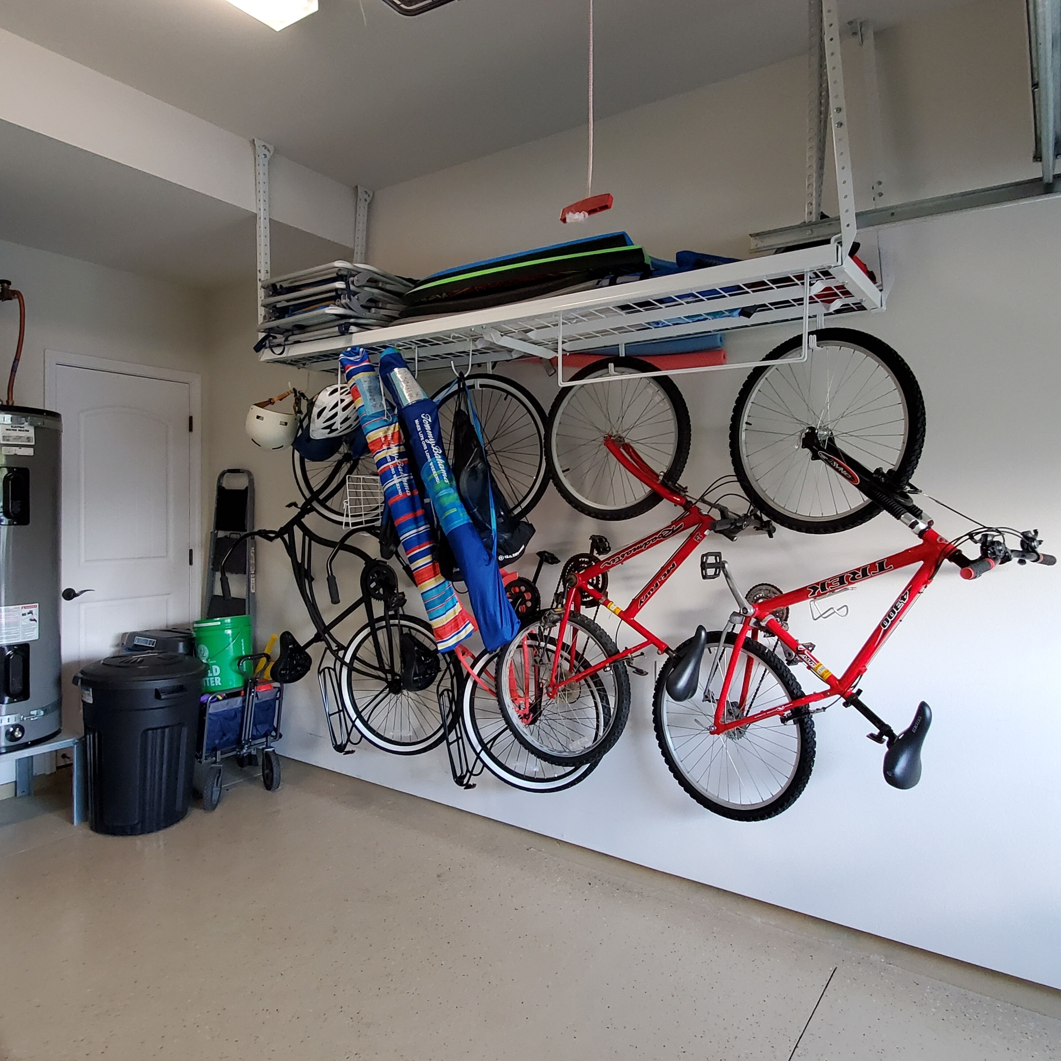Uma garagem com bicicletas fixadas na parede, um aquecedor e uma lata de lixo.