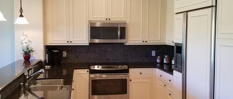 A modern kitchen with white cabinets, stainless steel appliances, a black backsplash, and a patterned rug.