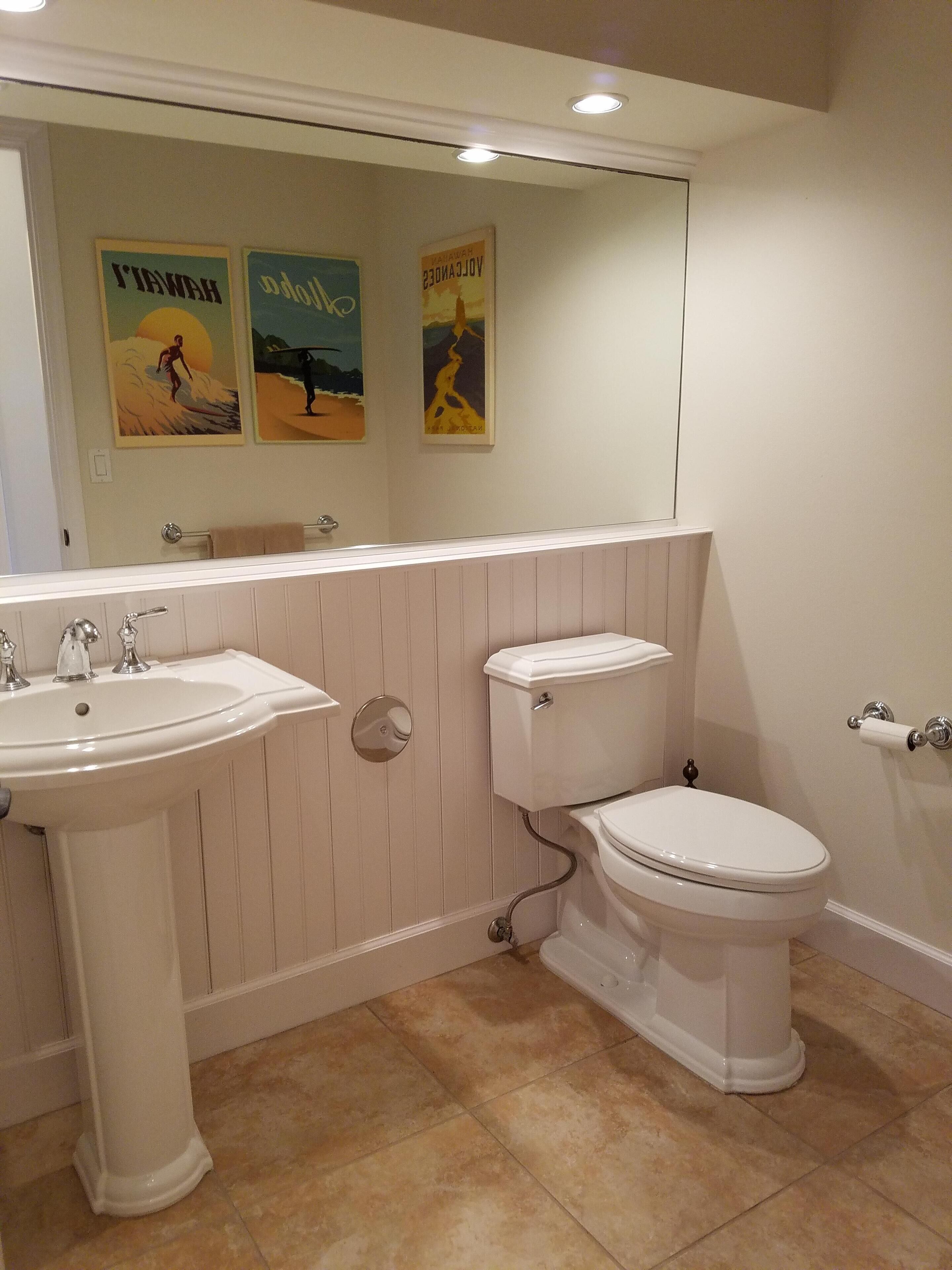 A bathroom with a sink, toilet, and mirror. There are three posters on the wall.