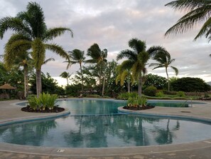 A pool area with palm trees, a lounge chair, and a small building in the background.