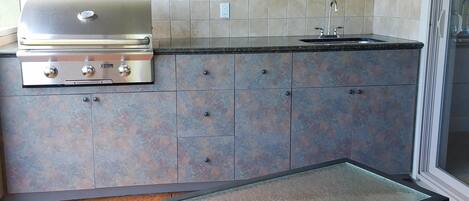 A kitchen with a built-in grill, a sink, and cabinets.