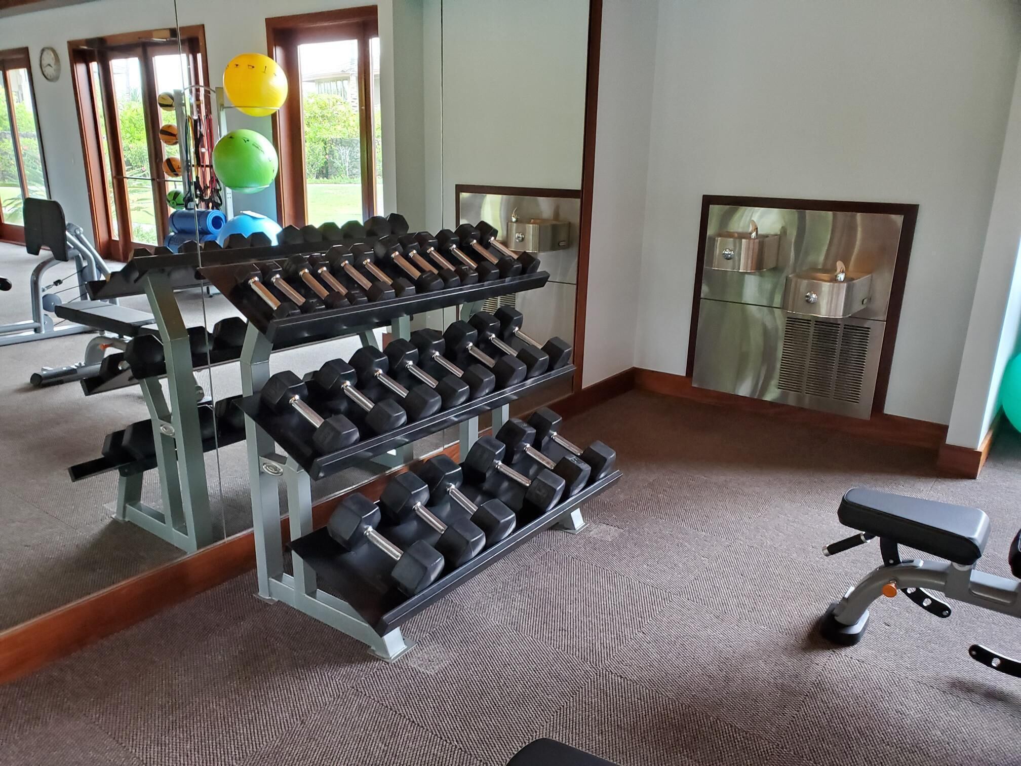 Un gimnasio con varios racks de mancuernas, una banca y pelotas de ejercicio.