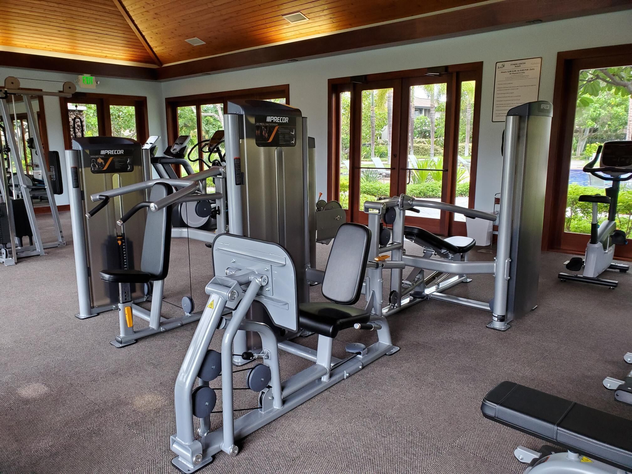 Ein Fitnessstudio mit verschiedenen Trainingsgeräten, Laufbändern und großen Fenstern mit Blick auf Grünflächen.