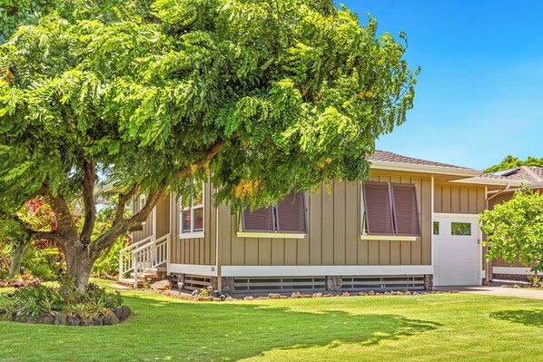 A single-story house with a front porch, a well-maintained lawn, and a large tree in the foreground.