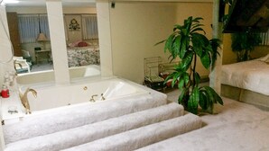 Un baño con bañera, ducha y lavabo. Hay una planta y un perchero para toallas.