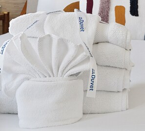 A stack of white towels with 'Duvet' branding, neatly folded and placed on a bed. - Whimsical Historic Retreat! | Globetrotter Suite C (Charleston)