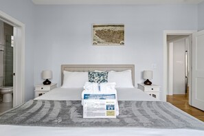 A neatly made bed with a welcome sign, a map on the wall, and a bathroom visible to the left. - Whimsical Historic Retreat! | Globetrotter Suite C (Charleston)