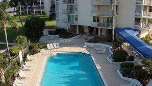 Ein Swimmingpool mit Liegestühlen und einem überdachten Bereich, umgeben von einer Hecke und Grünpflanzen.