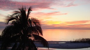 Ein Sonnenuntergang über einem Strand, Palmen sind als Silhouetten am Himmel erkennbar.