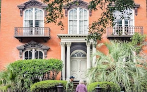 Stately brick building with a classic facade, featuring two-story windows and ornate balconies, set amidst manicured greenery.