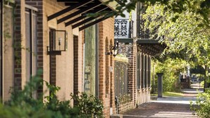A brick building with a covered walkway, outdoor lighting, and greenery. - Grand Manor on Broughton Street w/ Parking, Courtyard by Lucky Savannah (Savannah)