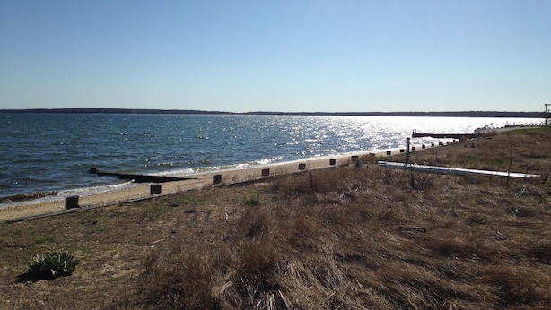 A coastal landscape with a clear sky, a sandy beach, and a grassy area with a fence and a telescope. - Beautiful North Fork 3-Bedroom Home Steps Away from a Private Sandy Bay (Southold)