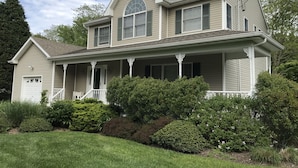 A two-story house with a front porch, a garage, and a well-maintained lawn. - Beautiful North Fork 3-Bedroom Home Steps Away from a Private Sandy Bay (Southold)