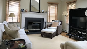 A living room with a fireplace, a sofa, a chair, a TV, and a coffee table. - Beautiful North Fork 3-Bedroom Home Steps Away from a Private Sandy Bay (Southold)