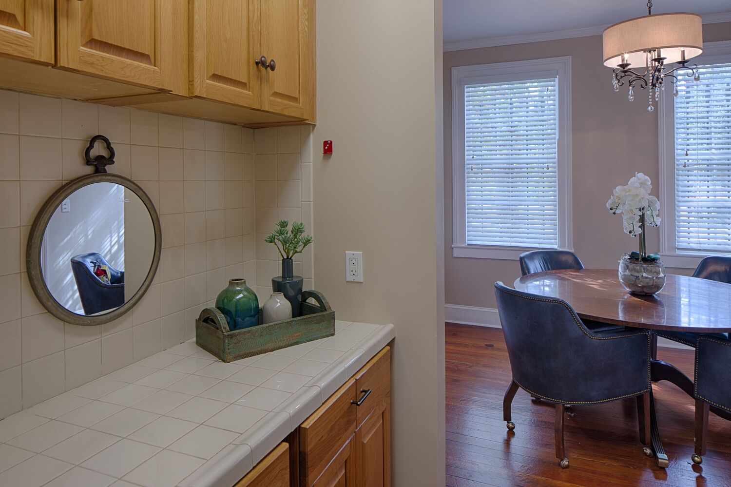 A kitchen with wooden cabinets, a tiled backsplash, a mirror, and a vase with plants.