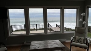 Una habitación con amplios ventanales que dan a una playa, una mesa de madera y una silla.
