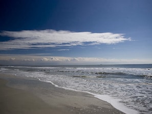 Une plage avec des vagues, un ciel dégagé et un navire à l’horizon.