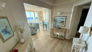 A spacious living area with a view of the ocean, a dining area with a table and chairs, and a console table with decorative items.