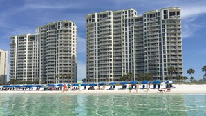 A beachfront hotel with multiple high-rise buildings, clear blue water, and beach umbrellas.