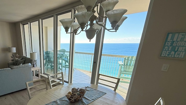 A spacious room with a large window overlooking the ocean, a dining table with chairs, and a chandelier.