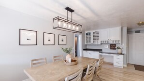 Une cuisine moderne avec des meubles blancs, une table à manger en bois et un luminaire suspendu.