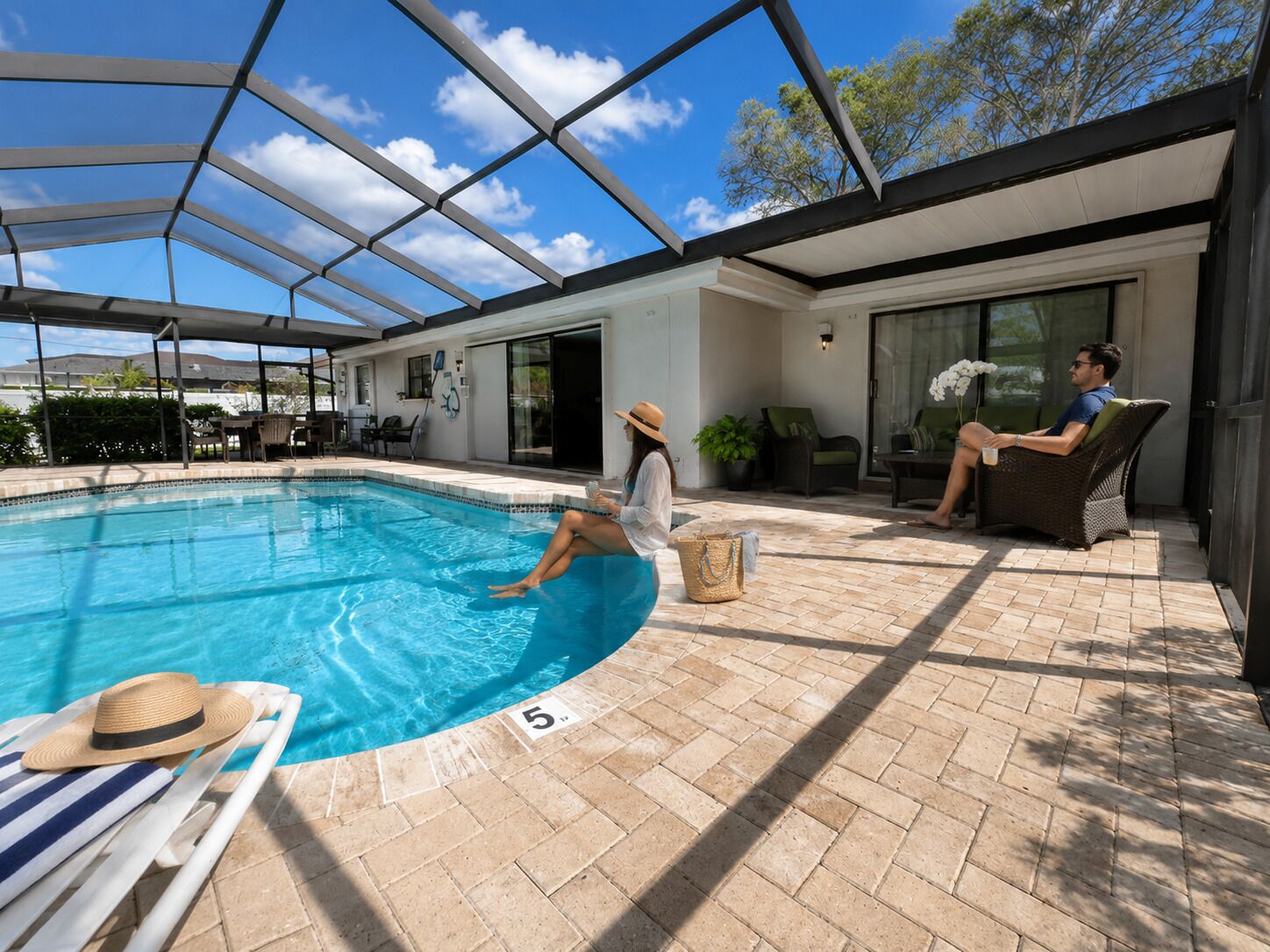 An indoor swimming pool with a covered area, lounge chairs, and a patio with a glass door.
