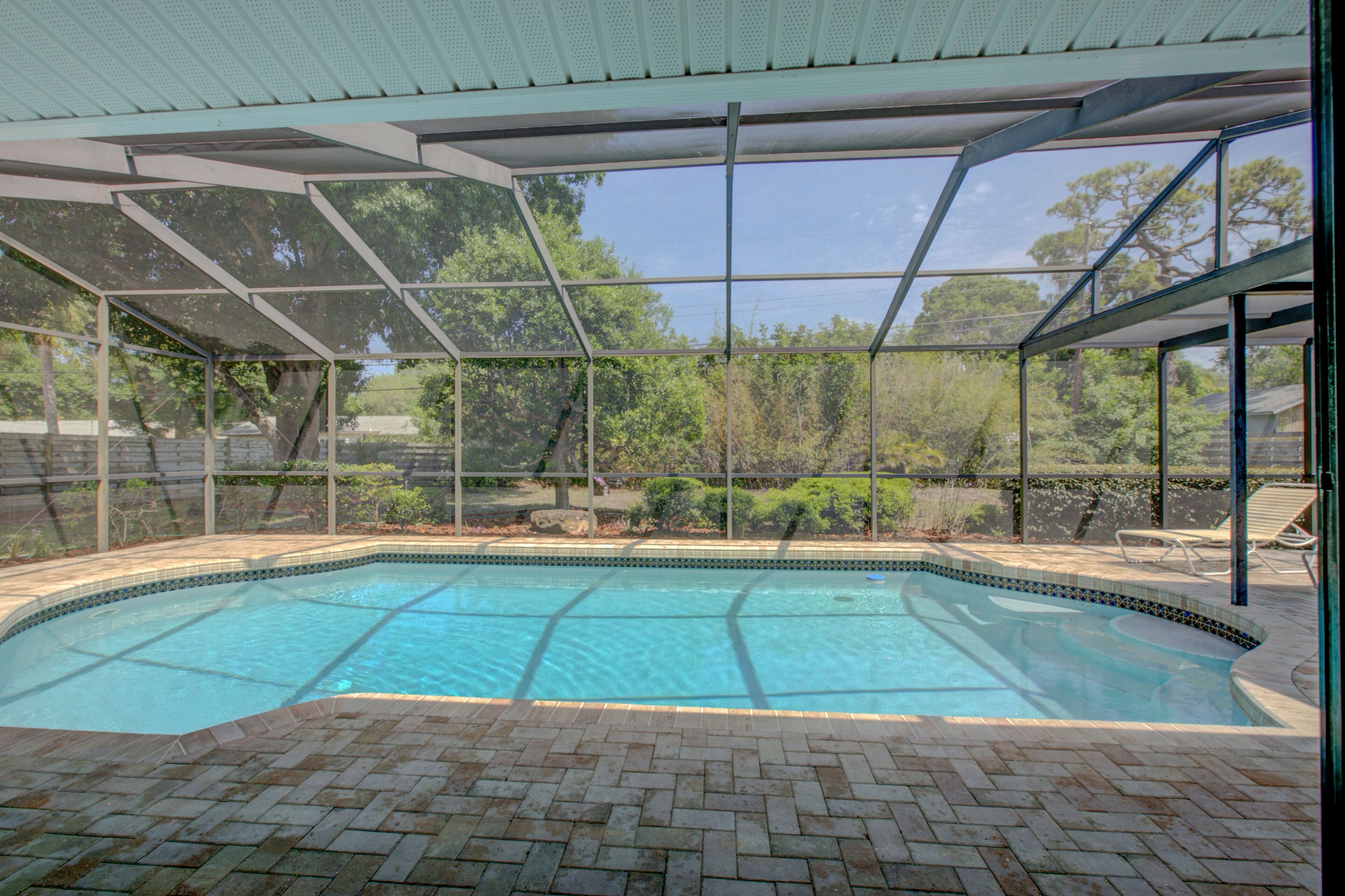 Une piscine couverte dotée d’une terrasse en briques, entourée d’une structure en verre et d’arbres.