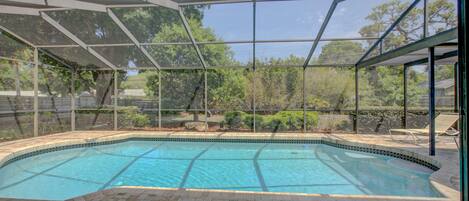 Une piscine couverte dotée d’une terrasse en briques, entourée d’une structure en verre et d’arbres.