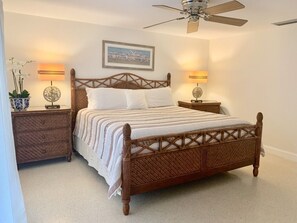 A bedroom with a wooden bed, two bedside tables with lamps, a ceiling fan, and a framed picture on the wall.