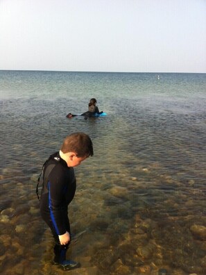 A person standing in shallow water with another person in the background.