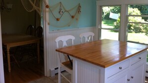 A kitchen with a wooden countertop, white cabinetry, and a view of the outdoors through large windows. - Beautiful 2 Bedroom Cottage Just Short Stroll To Town Neck Beach (Sandwich)