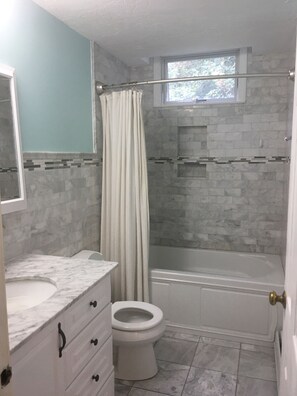 A bathroom with a marble sink, a toilet, a bathtub, and a shower curtain.
