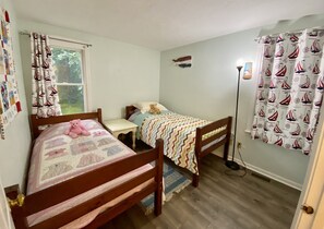 Quarto com duas camas de madeira, mesa de cabeceira, abajur e janela com cortinas.