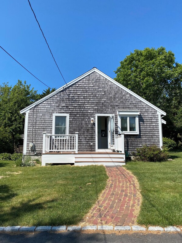 A single-story house with a front porch, a small attached garage, and a brick pathway leading to the entrance.