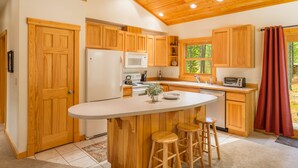 A kitchen with wooden cabinets, a central island with stools, a microwave, and a refrigerator.