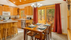 A wooden cabin kitchen with a dining area, wooden cabinets, a microwave, and a large window with curtains.