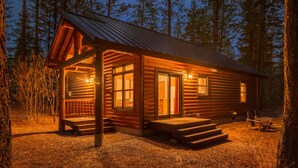 A wooden cabin with a porch, large windows, and a covered outdoor seating area.