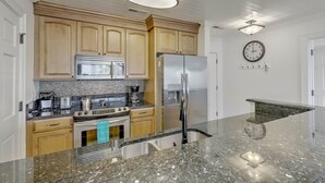 A kitchen with wooden cabinets, stainless steel appliances, a granite countertop, and a wall-mounted clock.