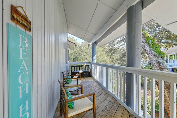 A covered porch with wooden chairs and a table, a 'BEACH' sign, and a view of trees and a house.