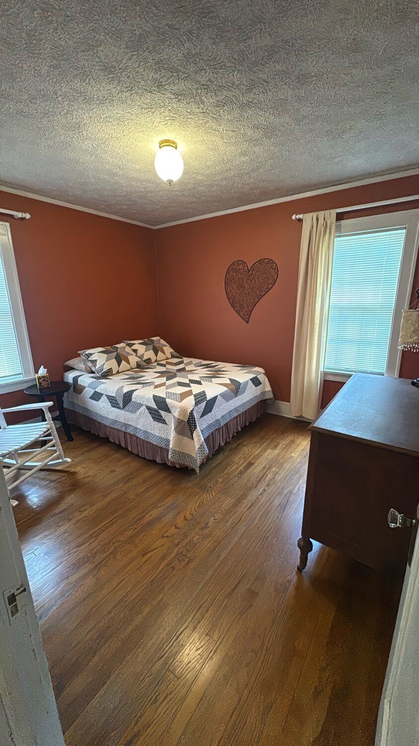 Ein Schlafzimmer mit einem Bett, einer Kommode, einem Schreibtisch und einer Wanddekoration in Herzform.