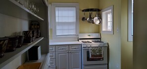 A compact kitchen with white cabinetry, a stove, and hanging pots. - Haven in Midtown's Historic Morton Meadows (Omaha)