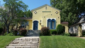 Una casa de dos pisos con un porche delantero, una puerta azul y un pequeño jardín.