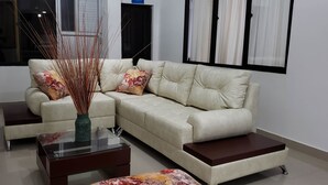 A modern living room with a beige sectional sofa, two side tables, and a decorative vase with tall stems. - Hotel San Blass (La Unión)